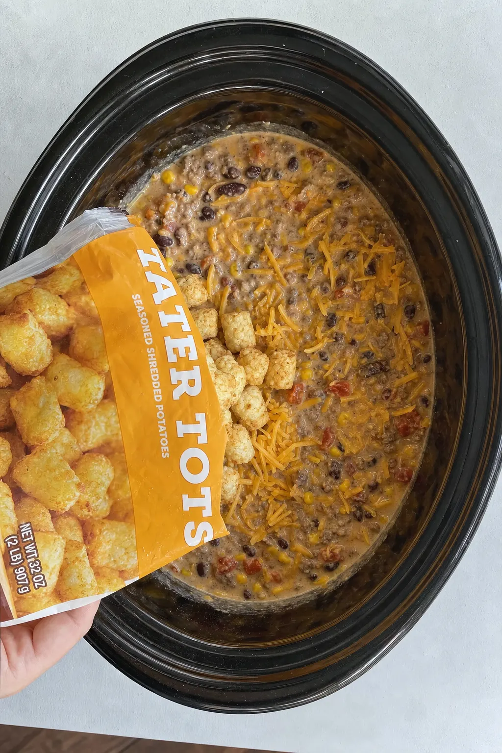 cowboy casserole beef mixture being assembled in slow cooker with corn beans and creamy sauce