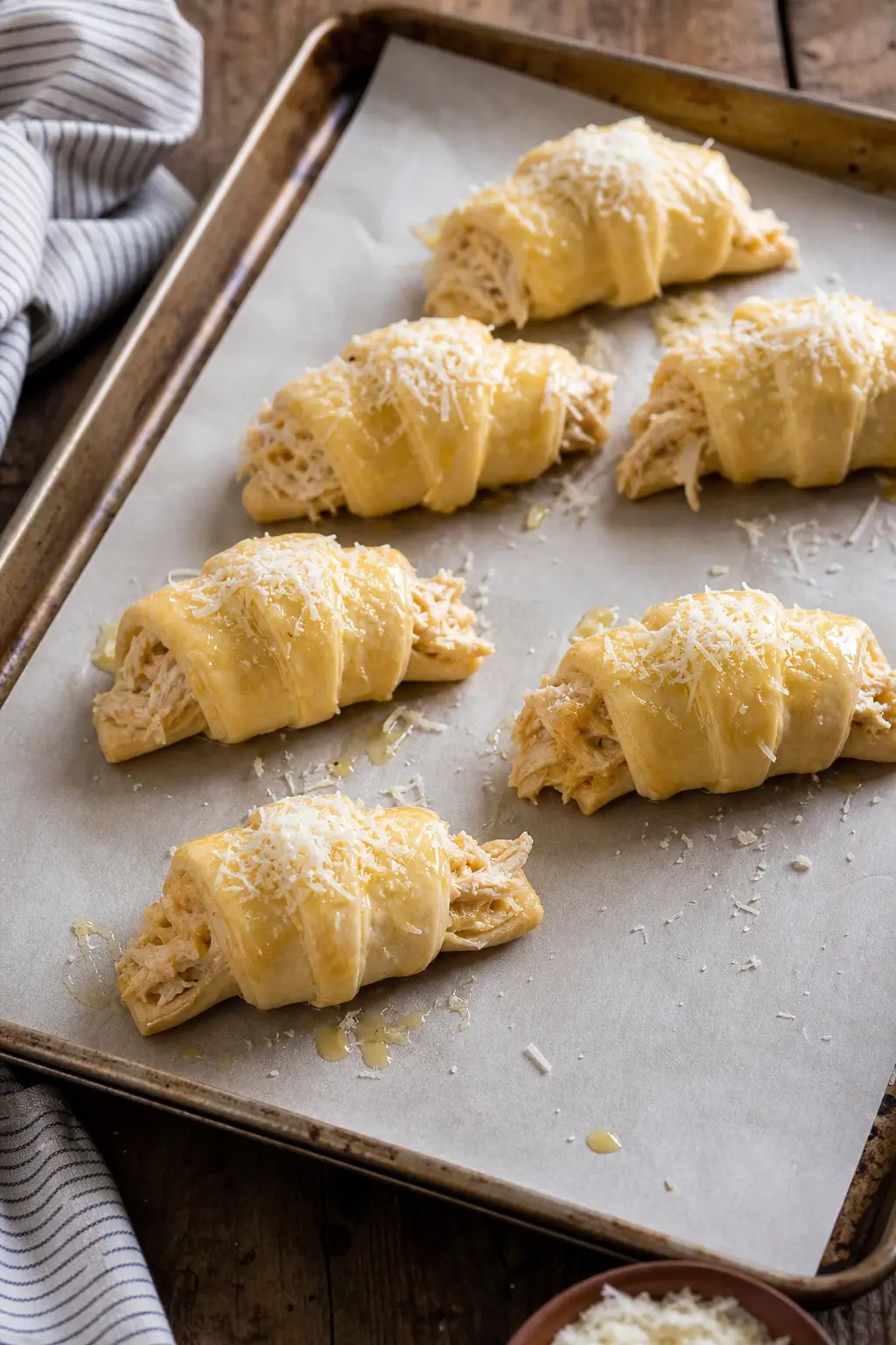cheesy chicken croissants brushed with butter and topped with parmesan ready to bake