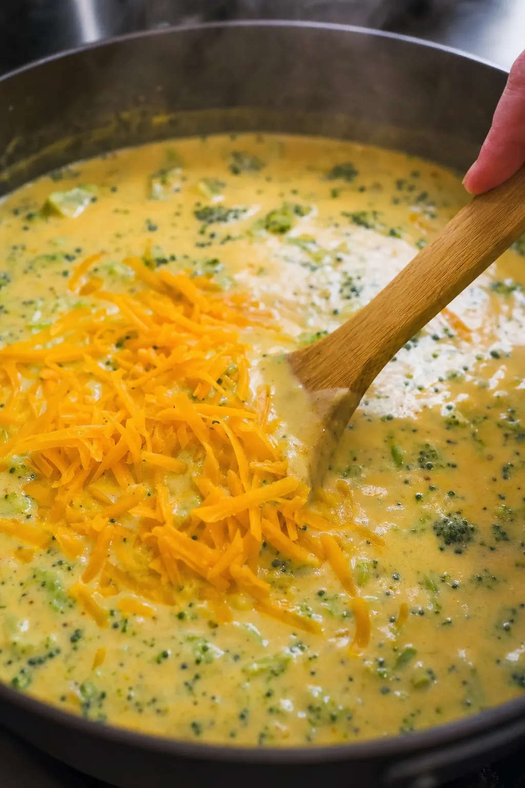 freshly grated sharp cheddar being stirred into broccoli soup turning it rich golden orange