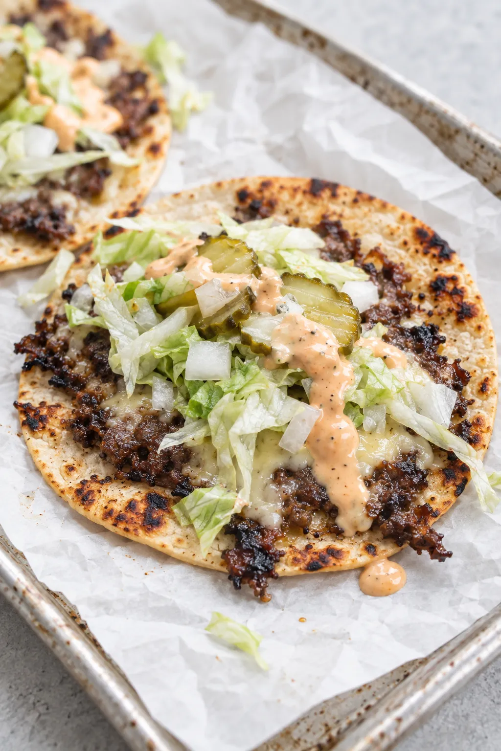 a finished smash burger taco on a plate topped with burger sauce, shredded lettuce, onion and pickles